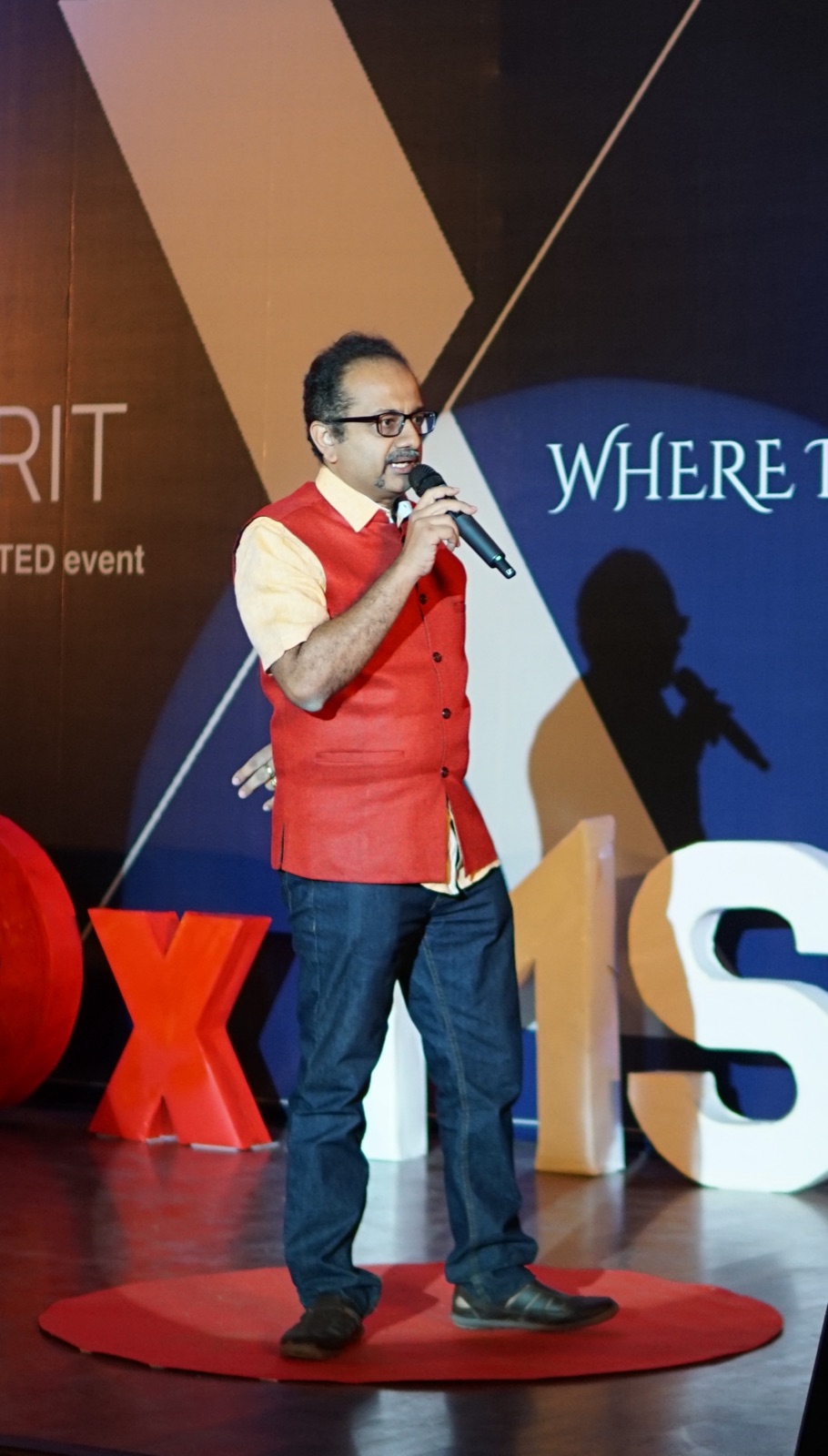 Sathya Sankaran on a TEDx stage in red Nehru jacket